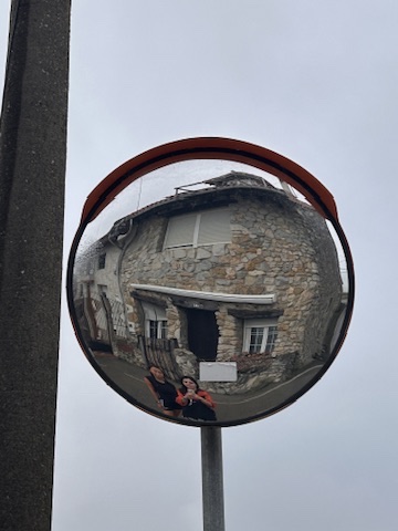 Dos caminantes reflejadas en un espejo junto a una casa de piedra